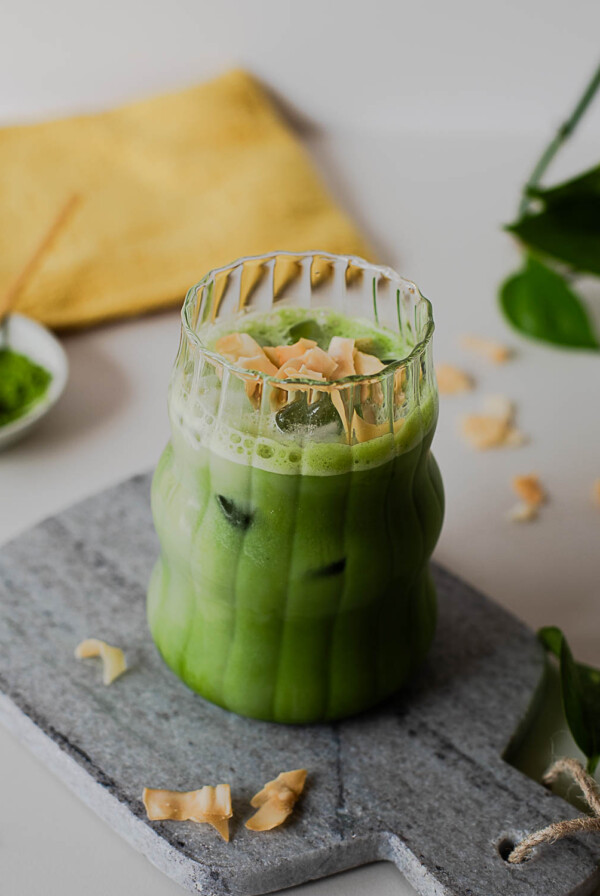 Coconut matcha latte with toasted coconut topping and layered green matcha tea in a glass over ice.