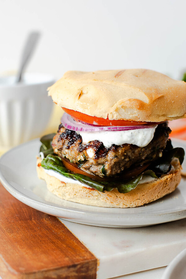 Mediterranean lamb burger topped with creamy dill yogurt sauce and fresh vegetables on a burger bun