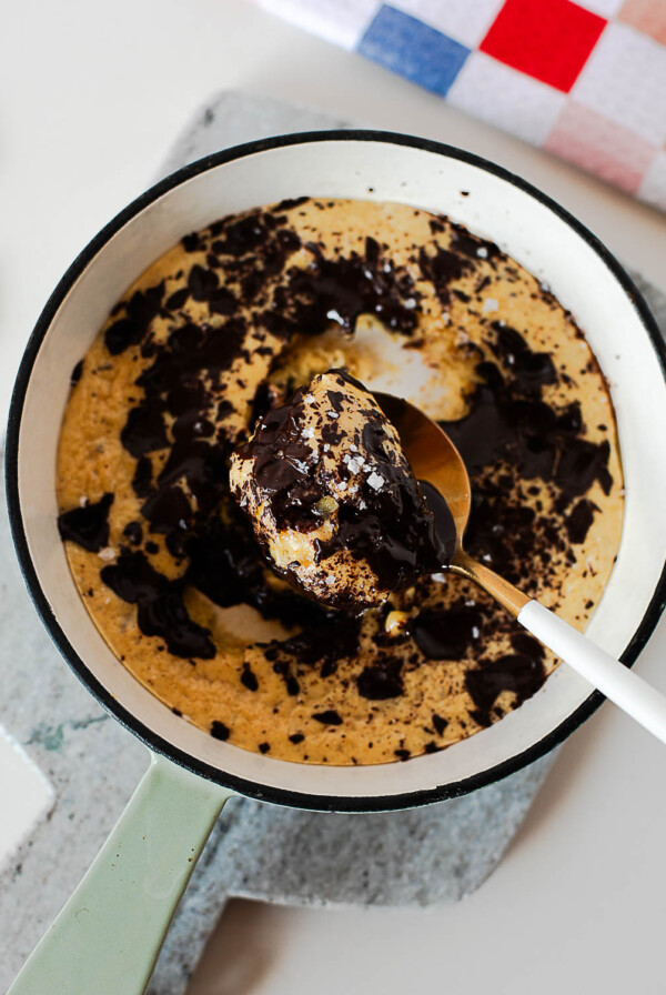 Spoon scooping into a gooey protein cookie skillet with melted dark chocolate and flaky sea salt on top.
