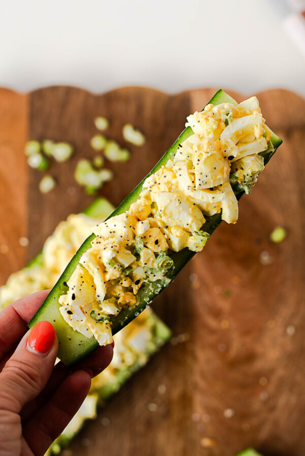 Hand holding a crunchy egg salad cucumber boat loaded with protein-packed egg salad and sprinkled with everything bagel seasoning.