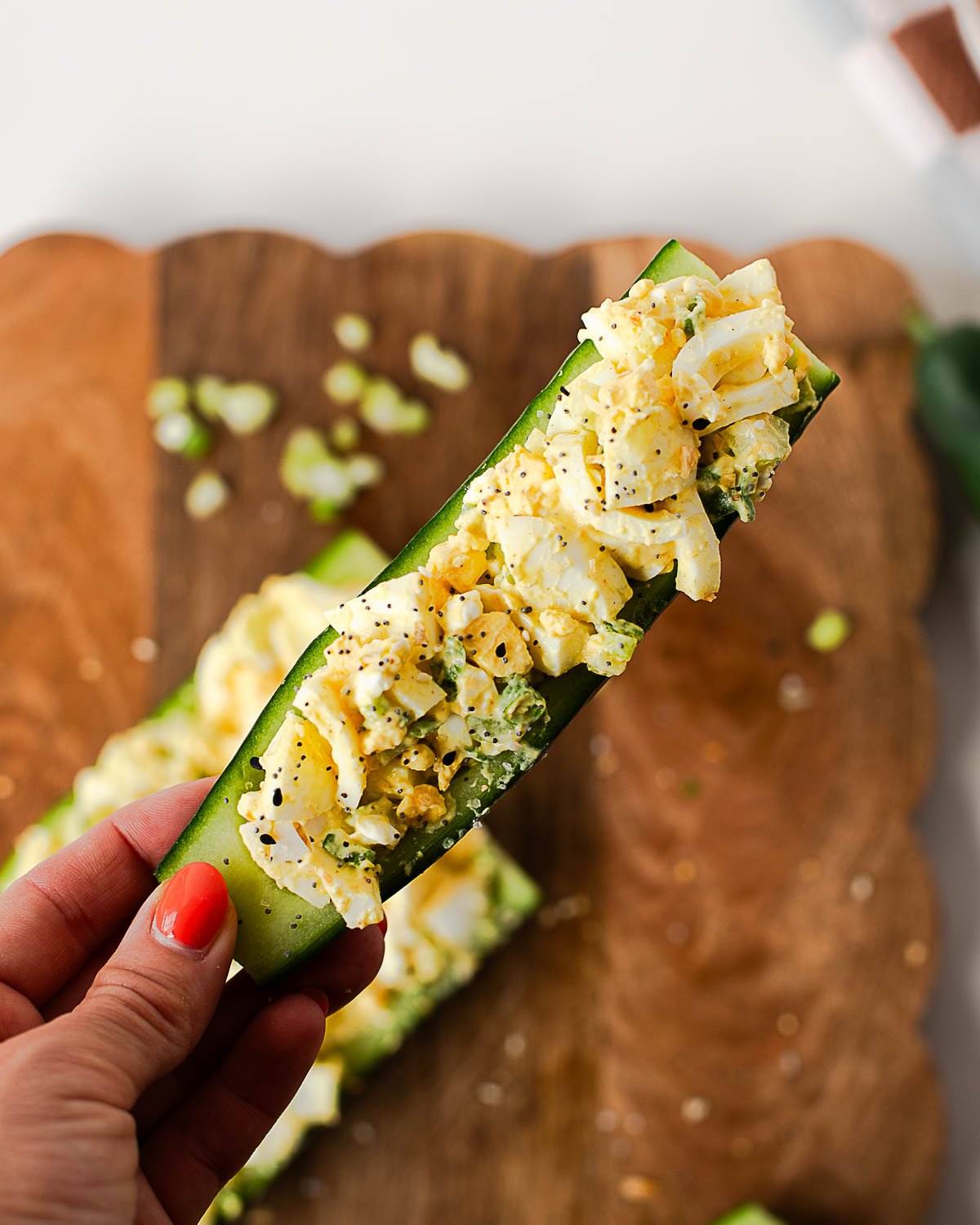 Hand holding a crunchy egg salad cucumber boat loaded with protein-packed egg salad and sprinkled with everything bagel seasoning.