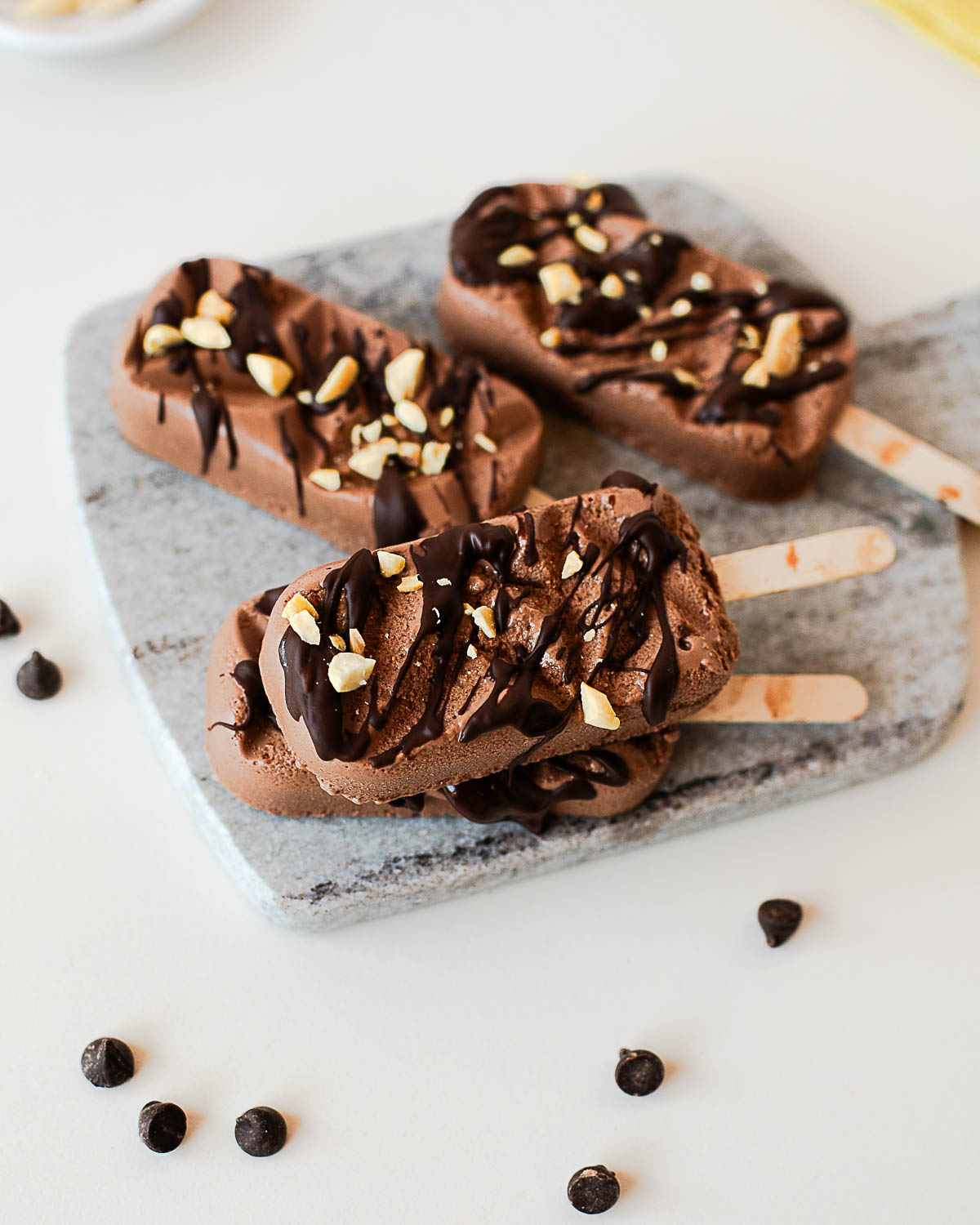 Creamy chocolate peanut butter protein popsicles drizzled with melted dark chocolate and topped with chopped peanuts on a stone serving board.