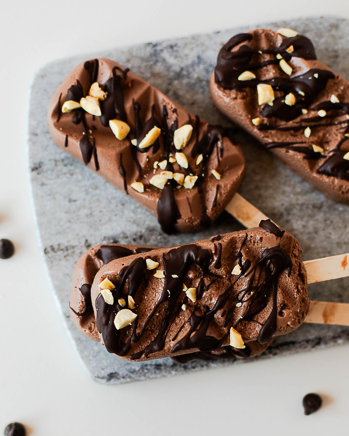 Chocolate protein popsicles topped with melted chocolate and chopped peanuts, featuring a rich, creamy texture and high-protein ingredients.