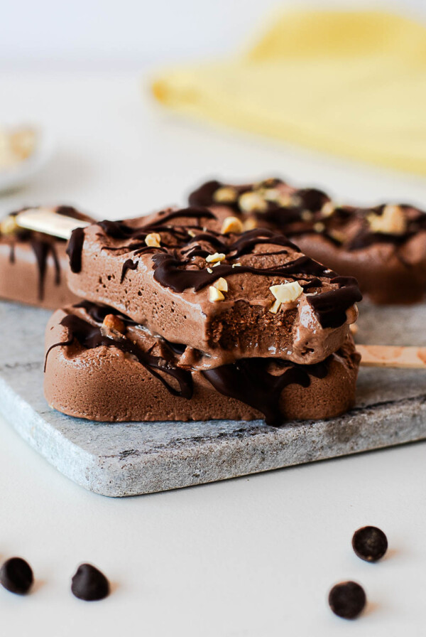 Bitten chocolate protein popsicle stacked on another popsicle, highlighting the smooth, creamy texture and chocolate peanut butter flavor.