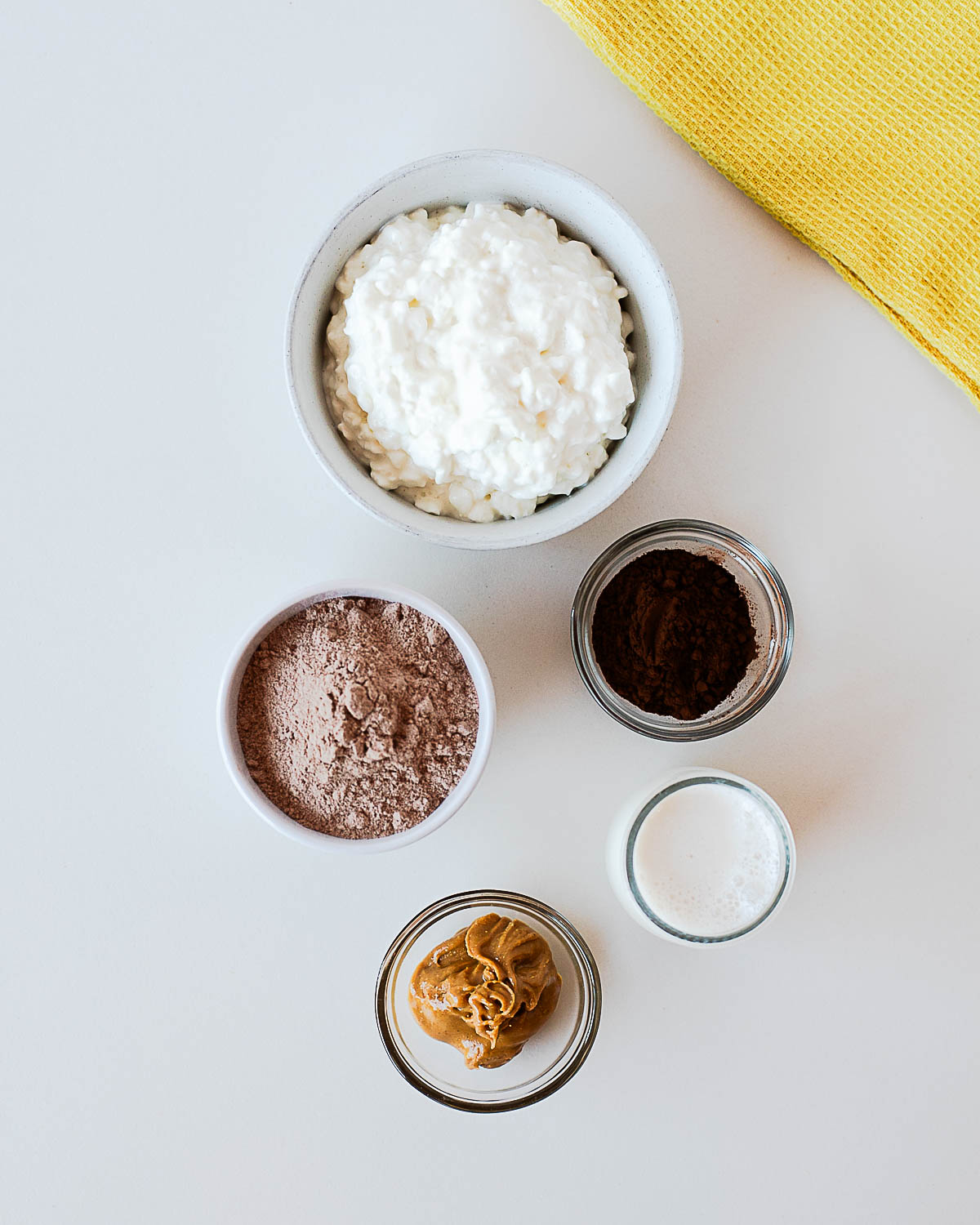 Ingredients for chocolate protein popsicles including cottage cheese, chocolate protein powder, peanut butter, cocoa powder, and almond milk laid out before blending.