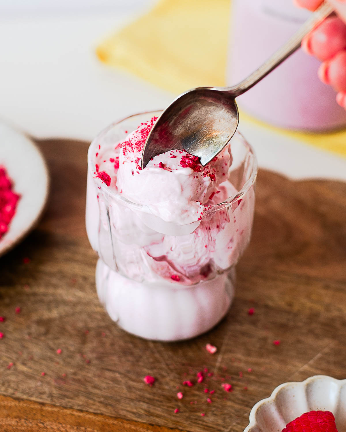 A spoon pressing into creamy raspberry protein ice cream topped with crushed freeze-dried raspberries, highlighting the smooth, scoopable texture.