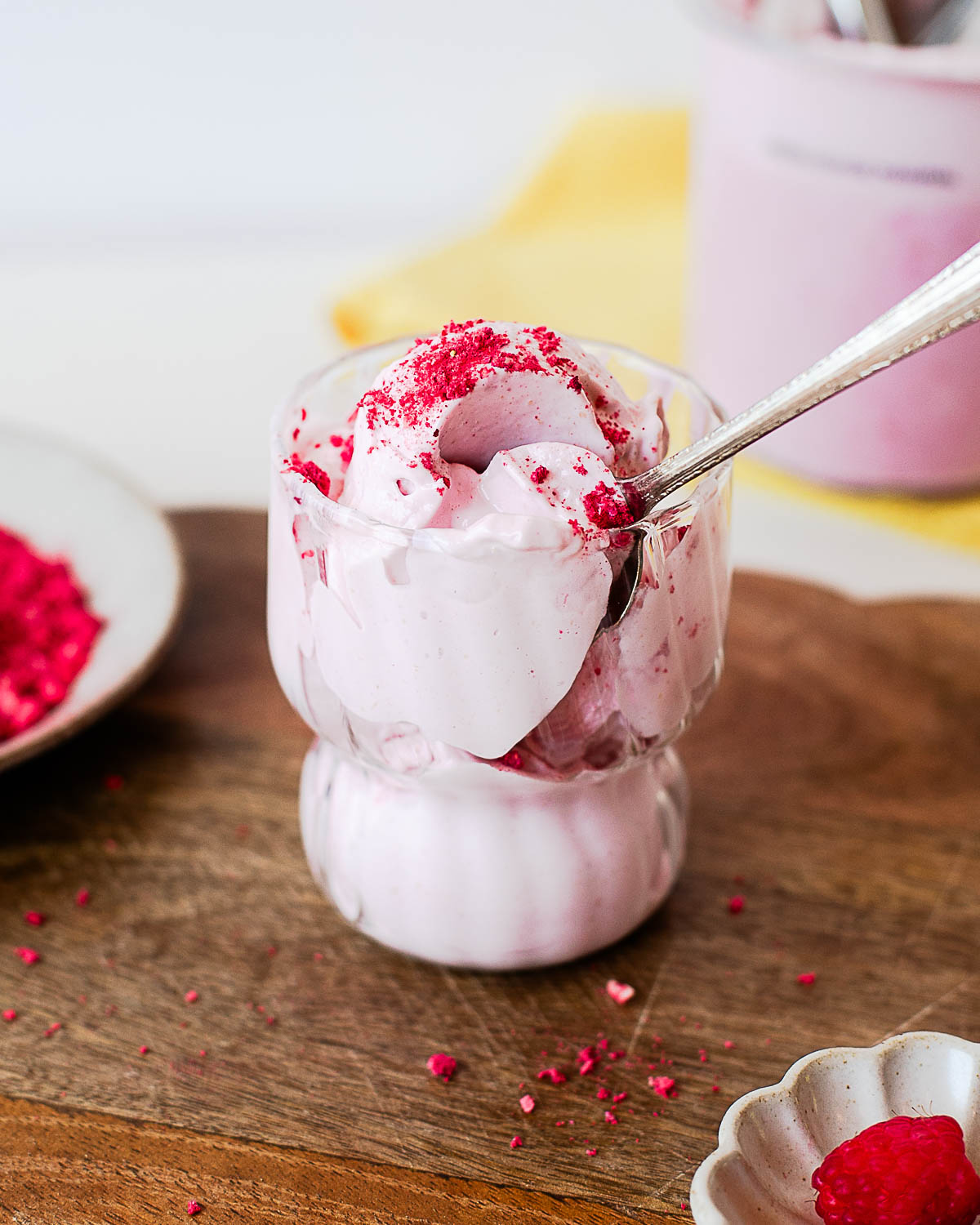 Close-up of a spoon scooping creamy raspberry protein ice cream from a glass dessert cup, topped with crushed freeze-dried raspberries.