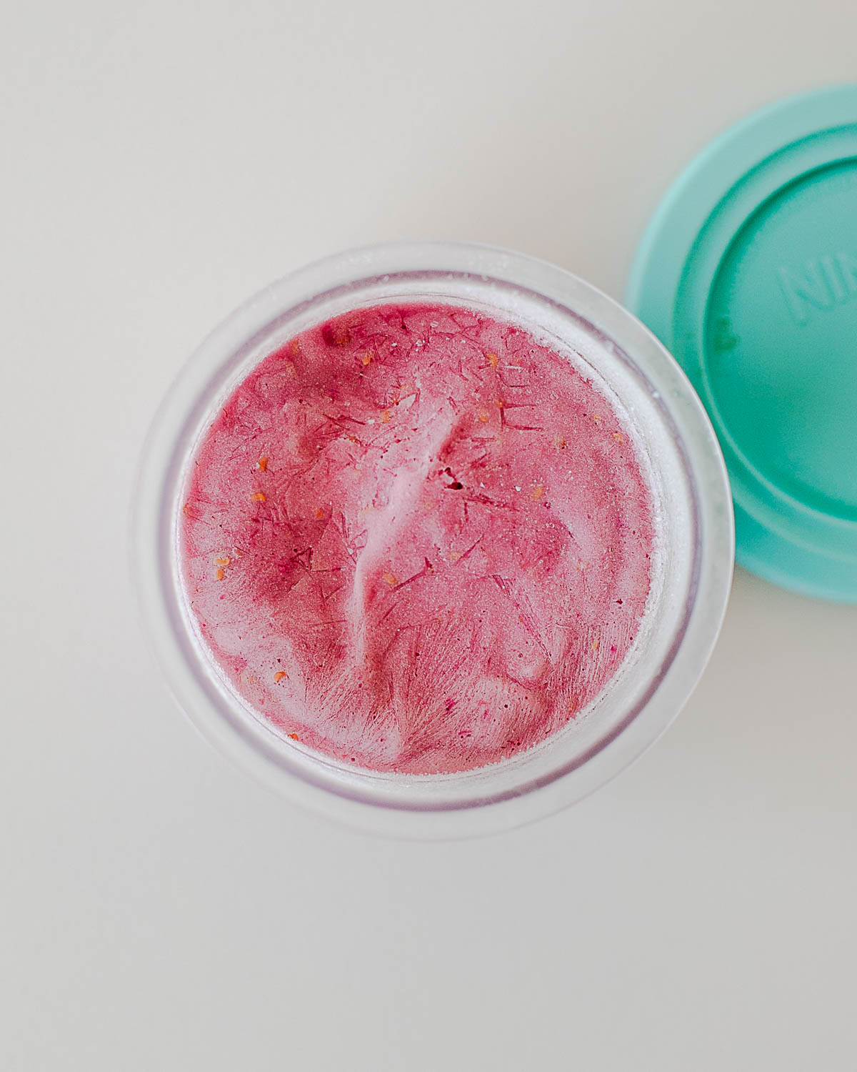 Frozen raspberry protein ice cream base in a Ninja Creami pint after freezing overnight, ready to spin into a creamy high-protein ice cream.