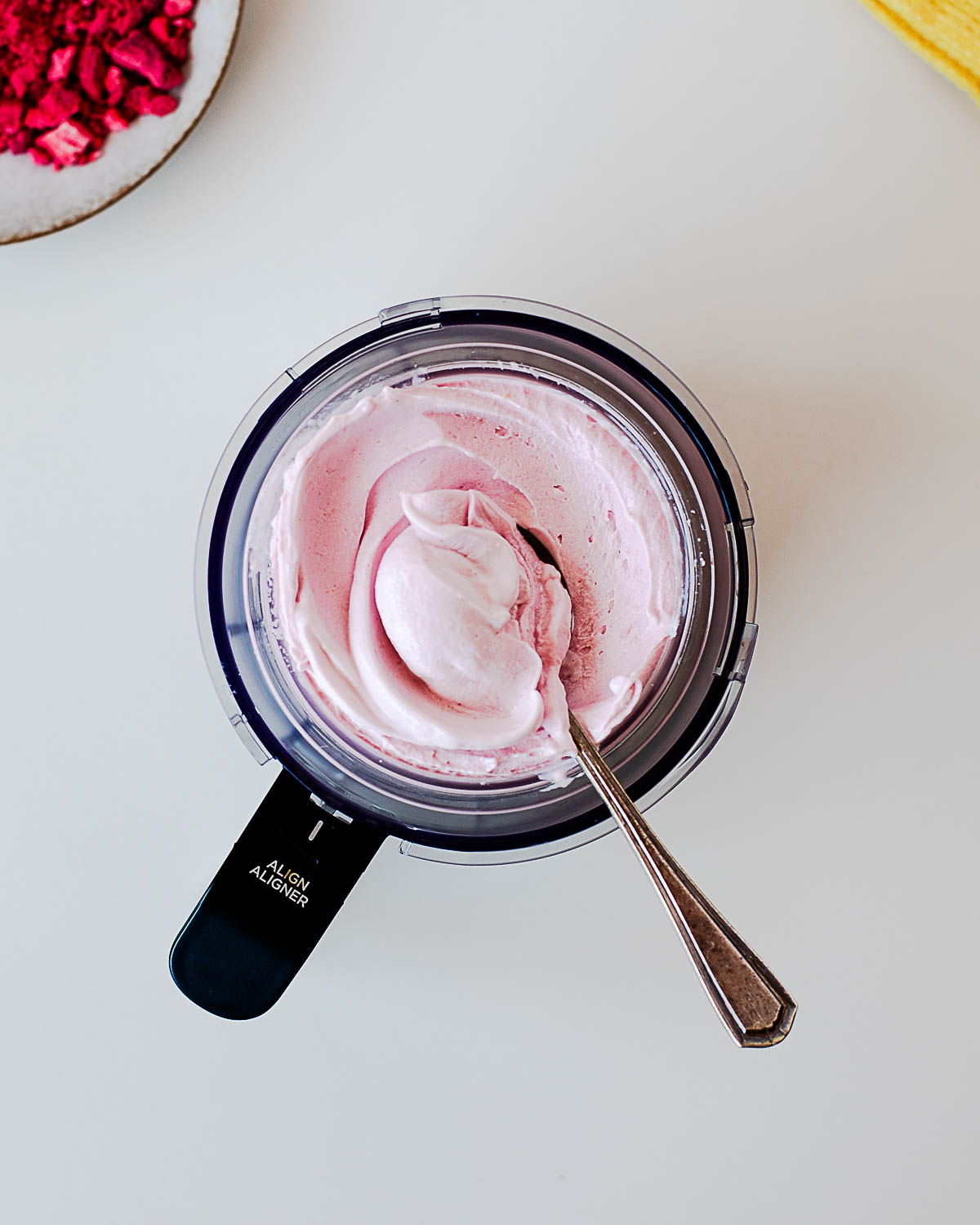 Freshly spun raspberry protein ice cream in a Ninja Creami pint with a spoon, showing its ultra-creamy, smooth texture after the Lite Ice Cream and Respin cycles.