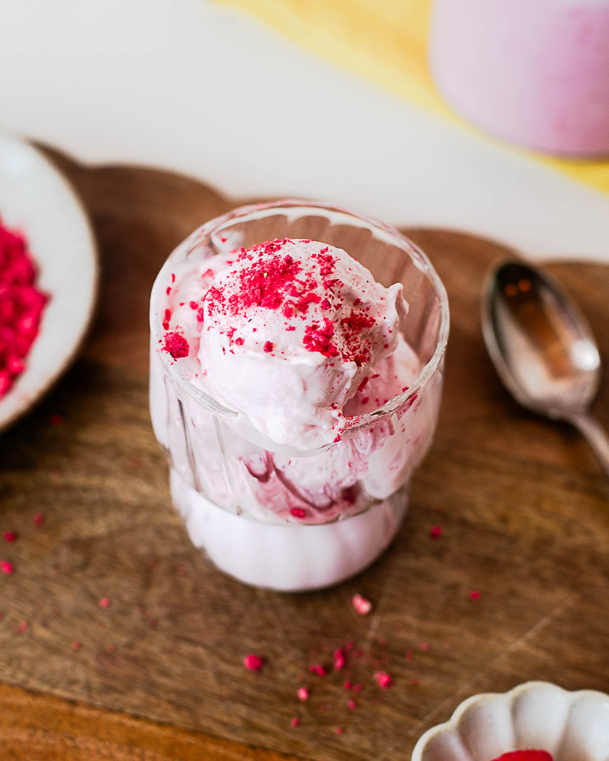 Close-up of homemade raspberry protein ice cream with a creamy texture, served in a glass bowl and topped with crushed freeze-dried raspberries.