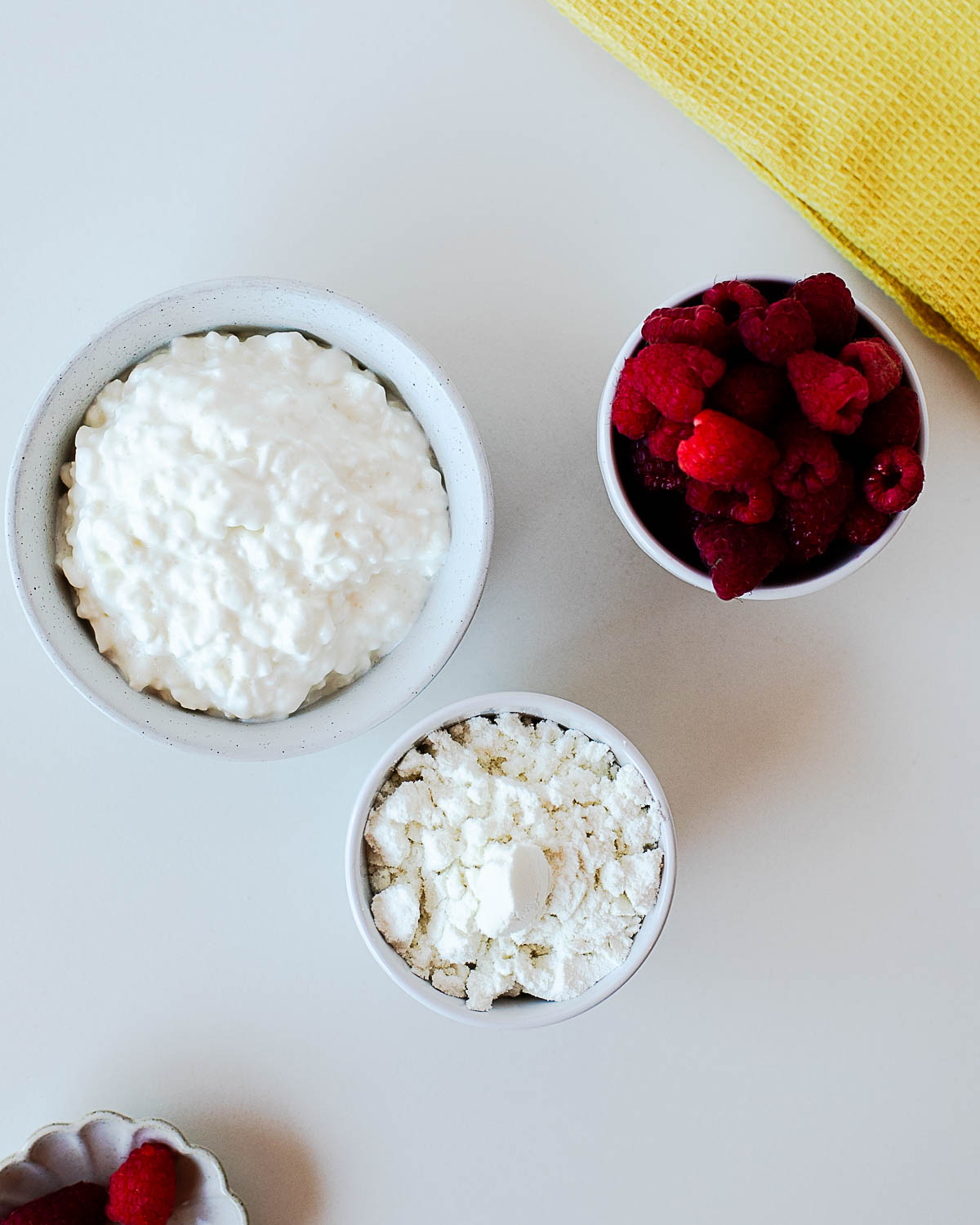 Simple ingredients for raspberry protein ice cream including cottage cheese, fresh raspberries, and vanilla protein powder arranged on a white countertop before blending.