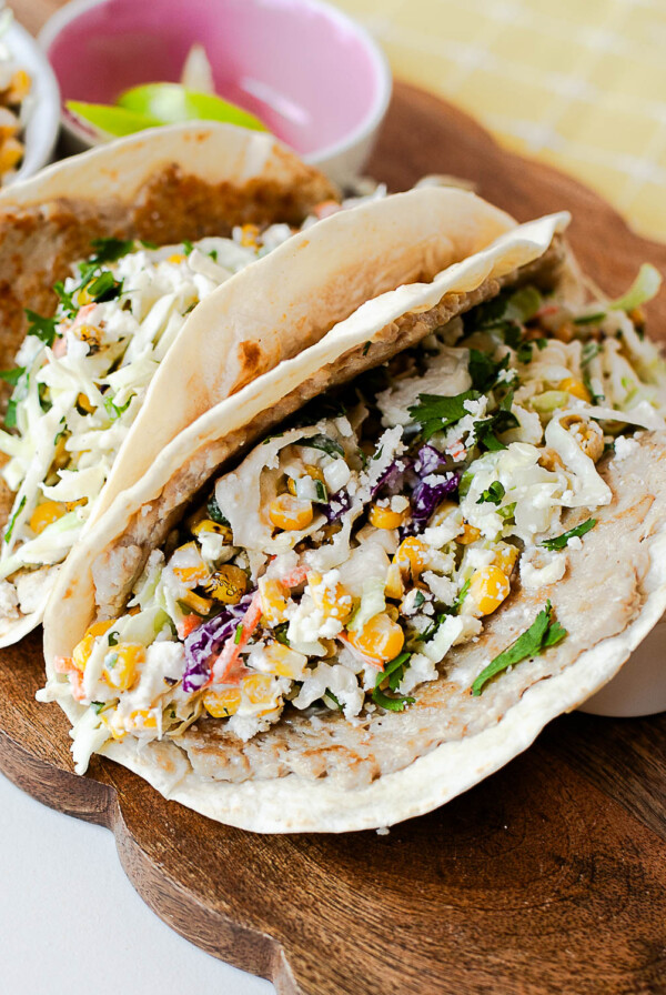 Street corn chicken smash tacos topped with creamy corn slaw, queso fresco, and fresh cilantro on a wooden serving board.