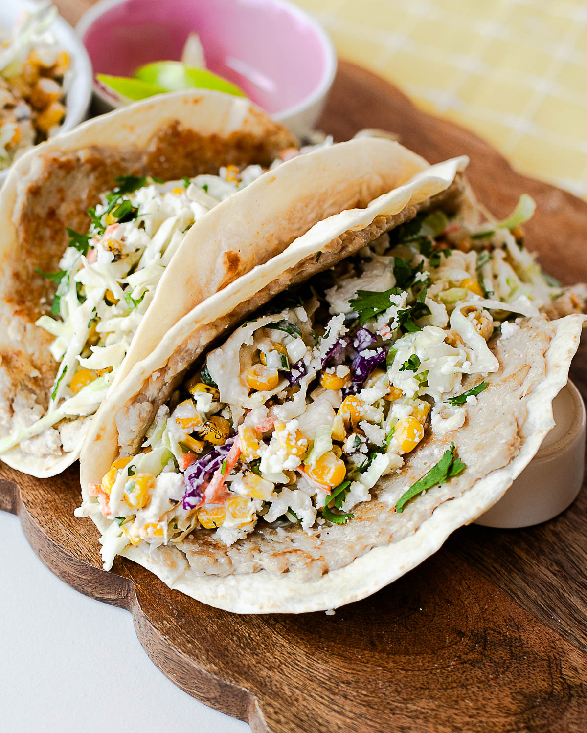 Street corn chicken smash tacos topped with creamy corn slaw, queso fresco, and fresh cilantro on a wooden serving board.