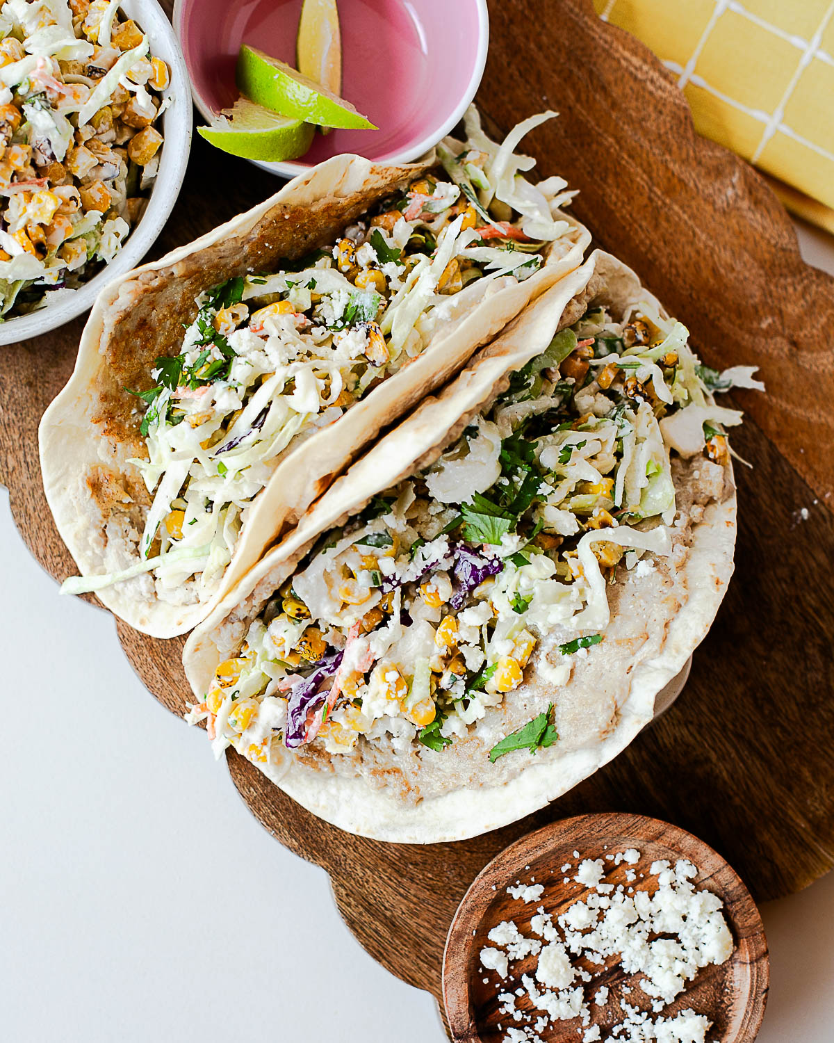 Overhead view of homemade street corn chicken smash tacos served with lime wedges and extra street corn slaw.