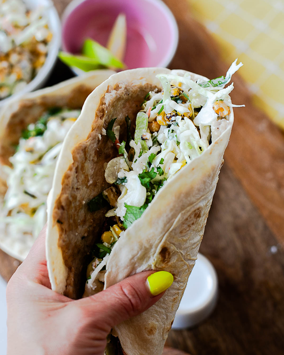 Hand holding a street corn chicken smash taco filled with creamy Mexican street corn slaw and crumbled queso fresco.